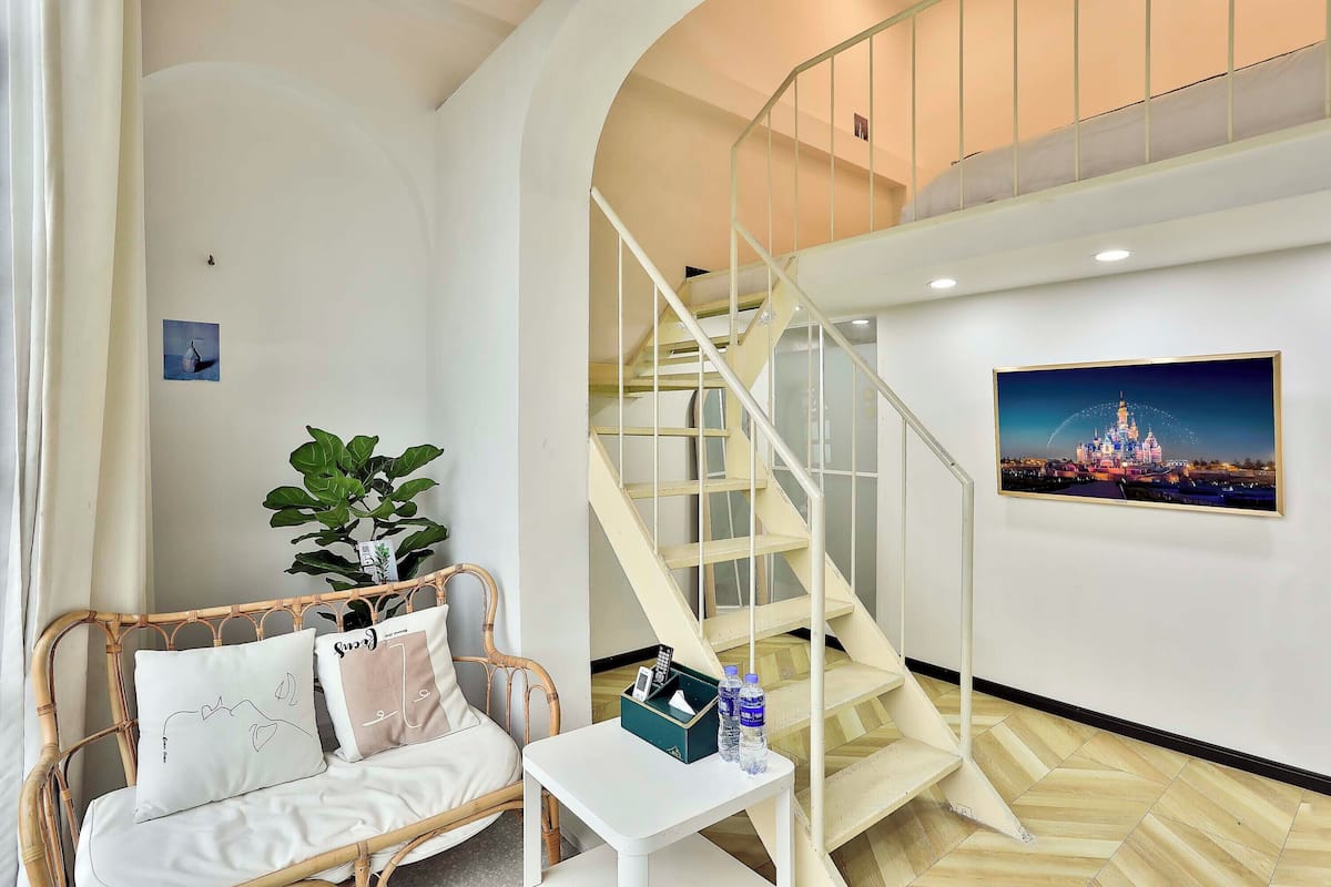 Un salon avec un canapé, une petite table, un escalier et un tableau encadré au mur.