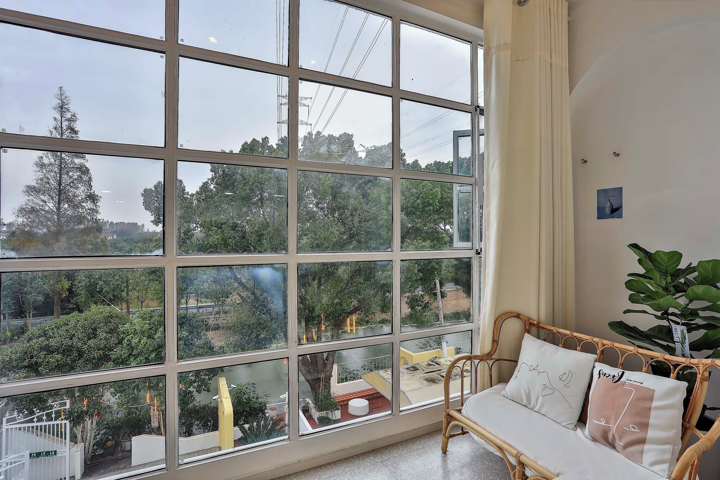 A room with a large window, a wicker sofa with cushions, and a potted plant.