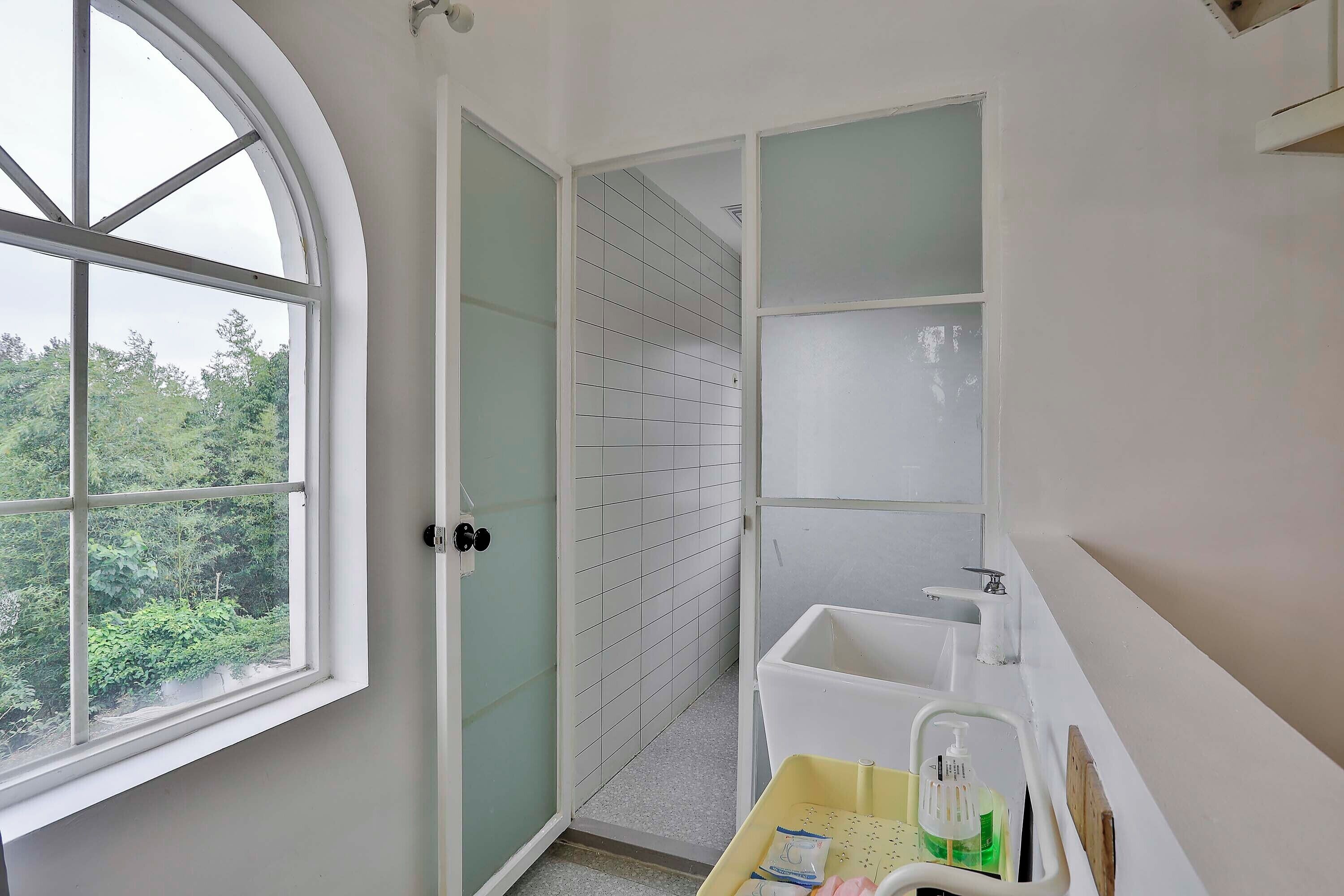 A bathroom with a white sink, a window, and a door leading to a tiled area.
