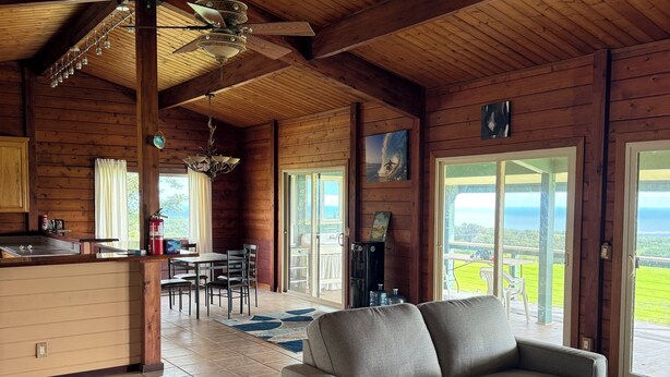 A spacious living area with a sofa, wooden floors, ceiling fans, and a view through large windows.