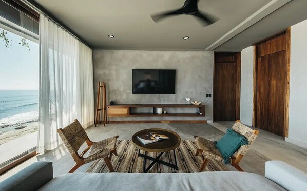 A modern living room with a large TV, wooden furniture, and a view of the beach. - Tankah Arthouse, Tulum Beachfront – Chef Included (Tulum)