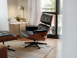 Uma sala de estar moderna com uma poltrona de couro preto, uma mesa redonda pequena com um abajur branco e um vaso de plantas.