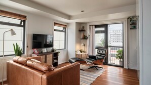 A modern living room with a leather sofa, a flat-screen TV, a dining table, and a balcony with a view of the city. - The Paloma by Homello | Quiet • Central • Perfect for Long Stays (Auckland)