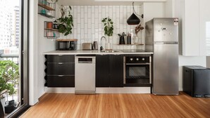 A modern kitchen with black and white cabinetry, a stainless steel refrigerator, a dishwasher, and an oven. There are plants on shelves and a hanging light fixture. - The Paloma by Homello | Quiet • Central • Perfect for Long Stays (Auckland)