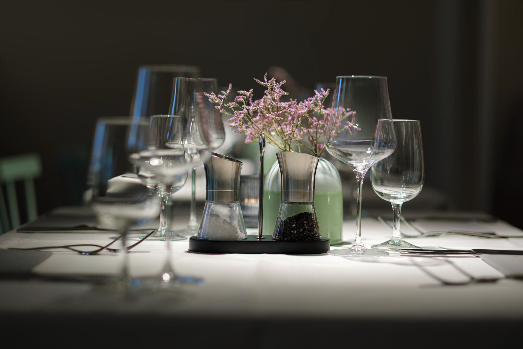A table set with various glassware, including wine glasses and a vase with flowers.