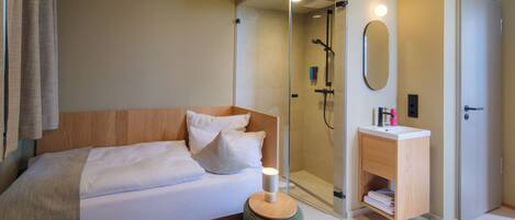 Une chambre à coucher moderne comprenant un lit, une table de chevet, un miroir, une douche à l’italienne et une armoire en bois.