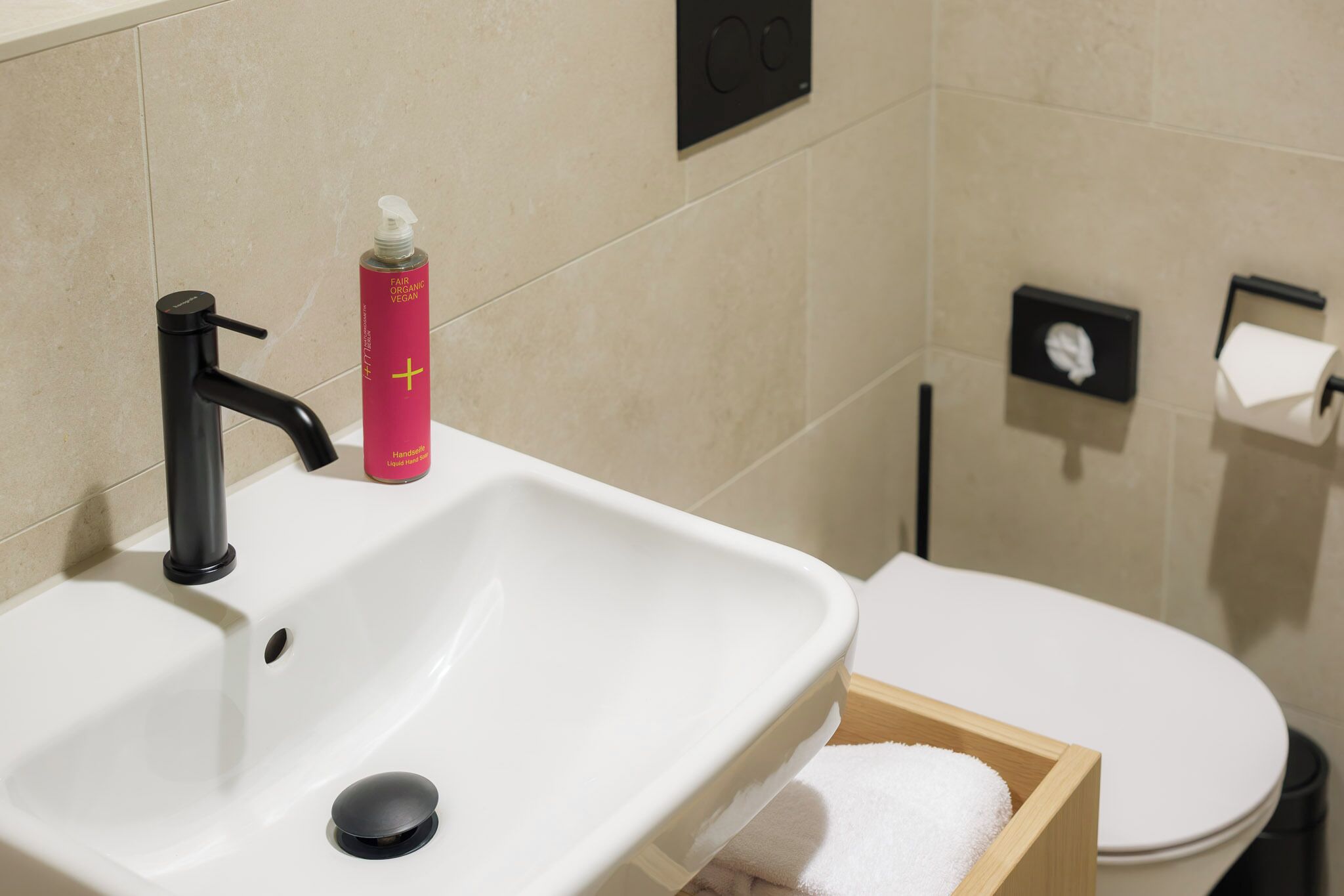 A bathroom with a white sink, black faucet, and a pink bottle of soap.