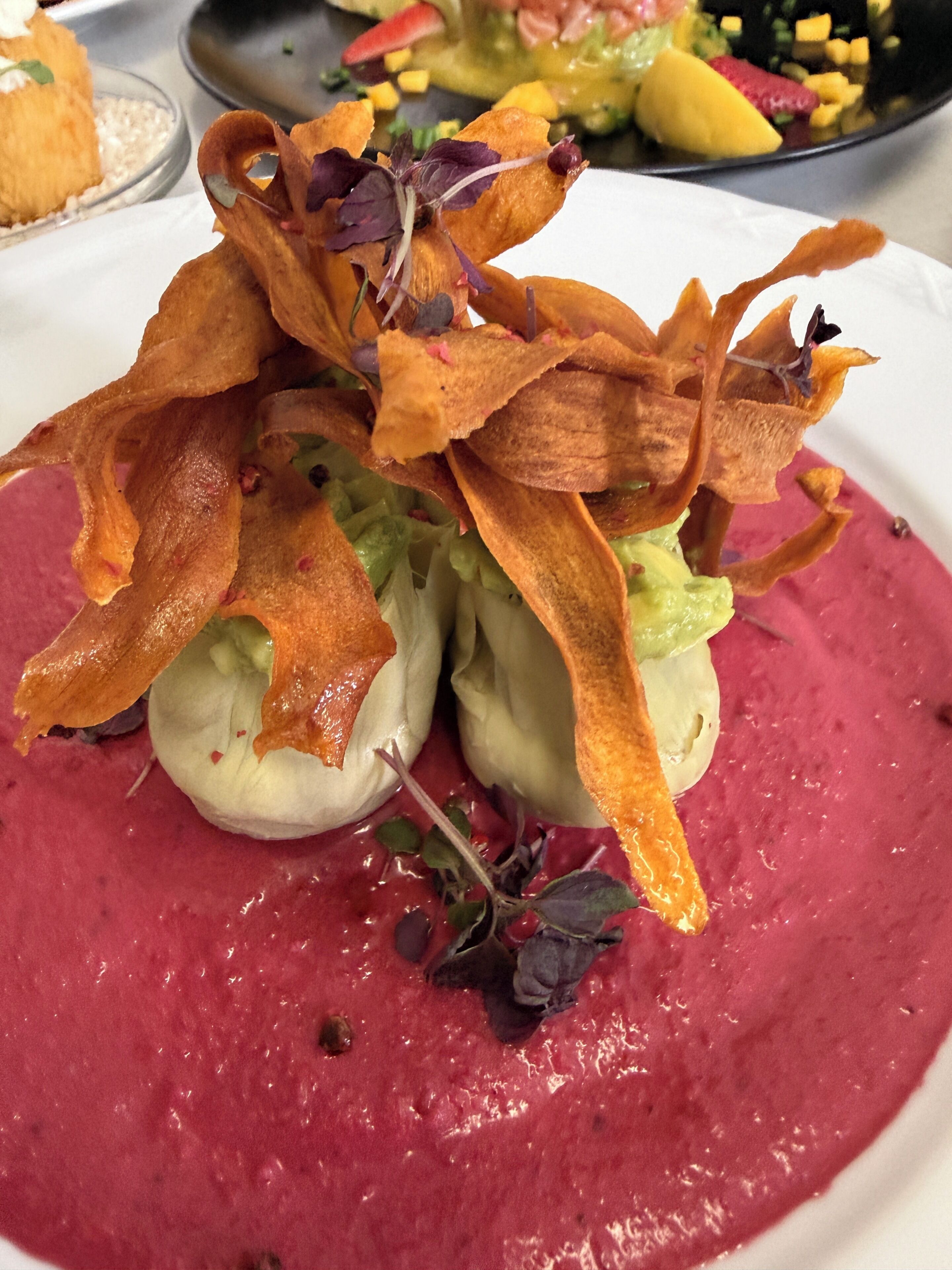 A dish with a vibrant red puree, garnished with crispy elements and microgreens.