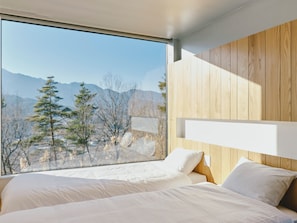 A bedroom with a large window, wooden panel wall, and a bed with white bedding. - BLANC YATSUGATAKE (Hokuto)