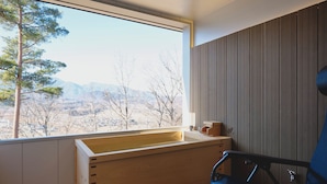 A room with a wooden bench, a chair, a window with a view of trees and mountains, and a wooden wall panel. - BLANC YATSUGATAKE (Hokuto)