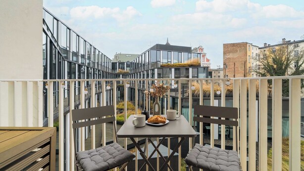 A balcony with a table set for two, a vase with dried flowers, and a plate of croissants.