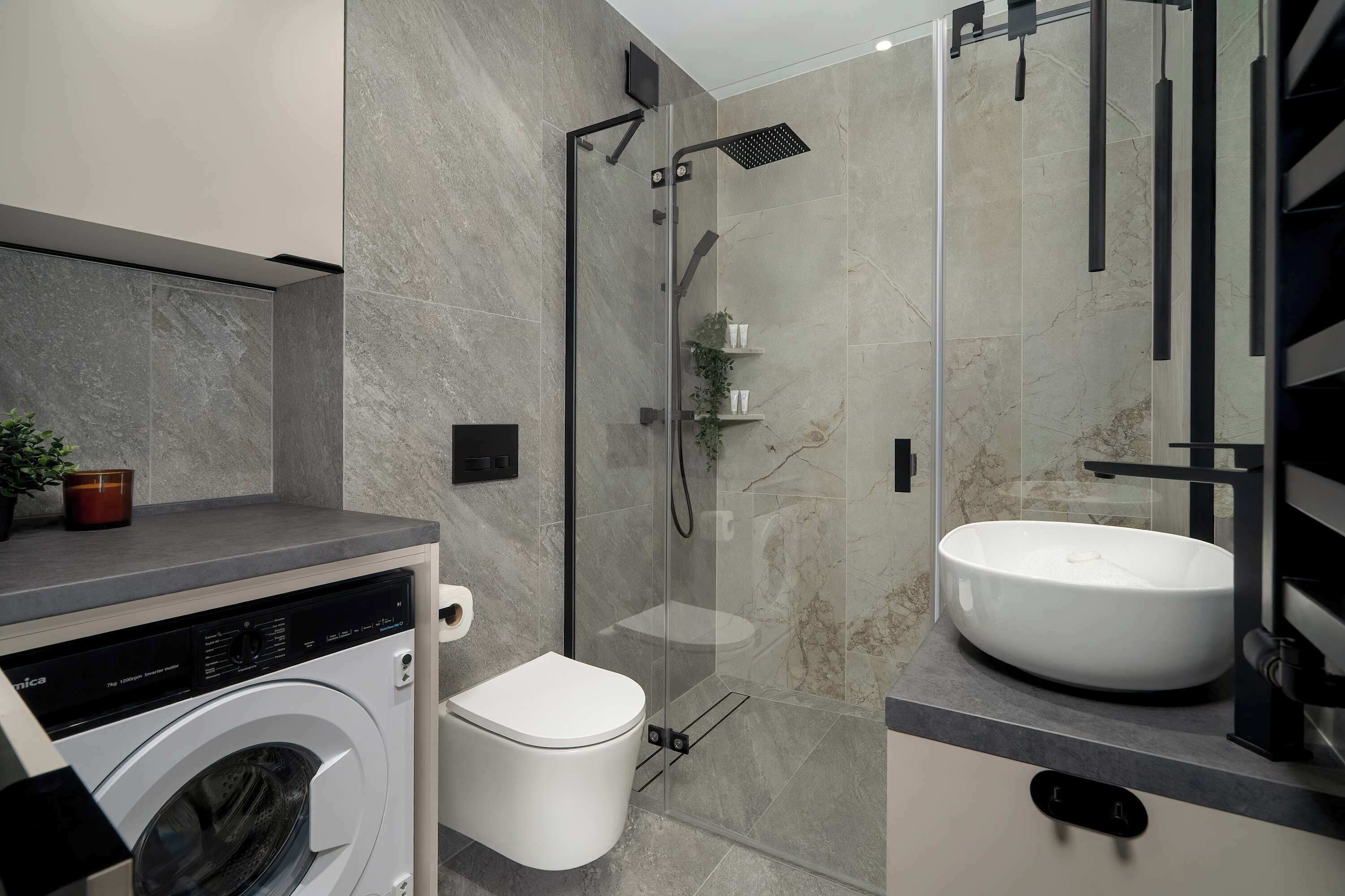 Un baño moderno con ducha envuelta en vidrio, lavamanos integrado y lavadora.