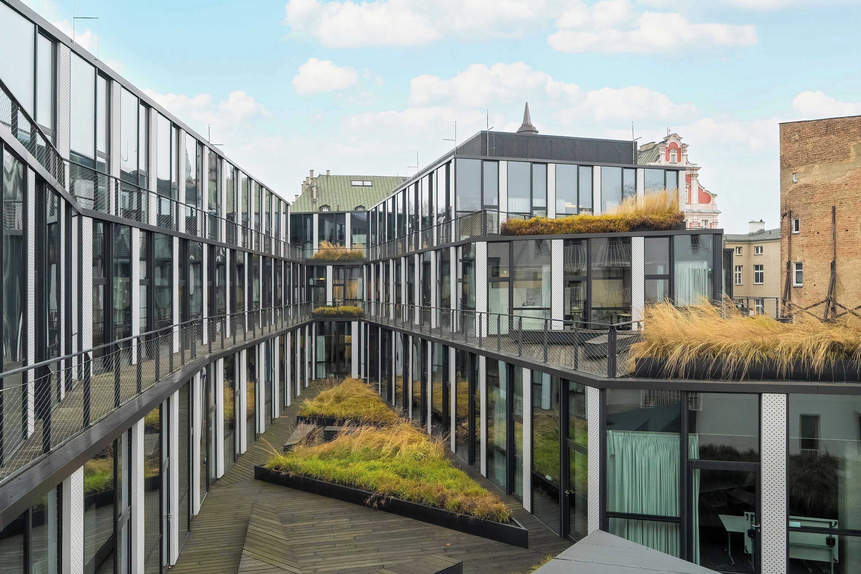 Een modern gebouw met een glazen gevel, een centraal atrium met een houten terras en een dakbostuin.