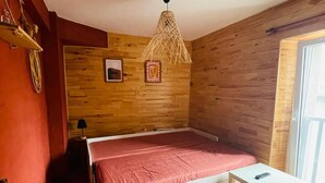A bedroom with a bed, a small table, a hanging light fixture, wooden walls, and a window. - Charming cottage (Marignac)