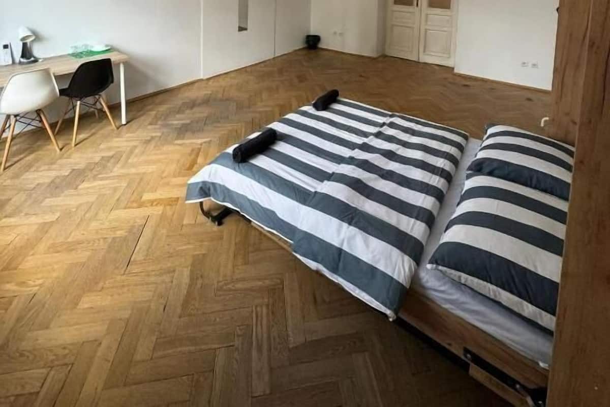 Una habitación con piso de madera tipo espiga, una cama con ropa de cama a rayas, un escritorio con silla y tres lámparas colgantes.