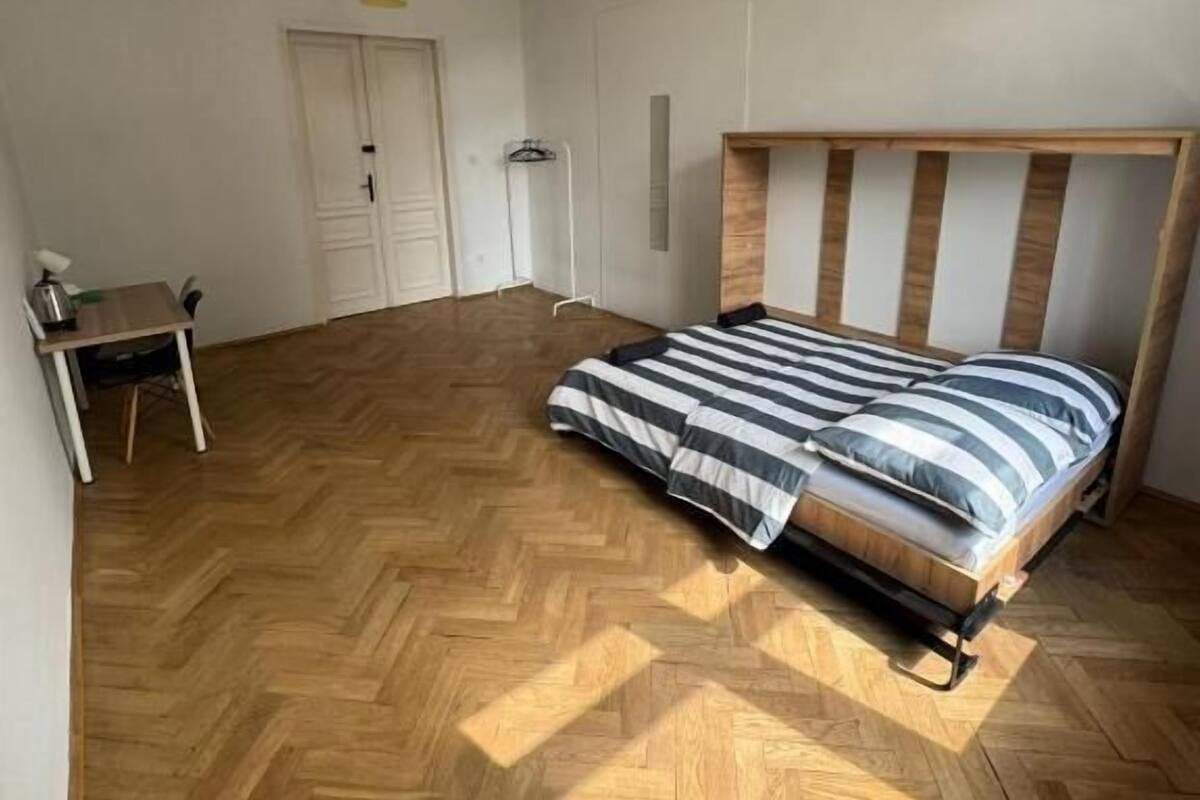 Un dormitorio con suelo de parqué tipo espiga, una cama con ropa de cama a rayas y dos lámparas colgantes.