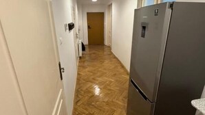 A narrow hallway with a wooden herringbone floor, a stainless steel refrigerator, and a door on the left. - Fantastic Inn Kraków - Krasińskiego (Kraków)