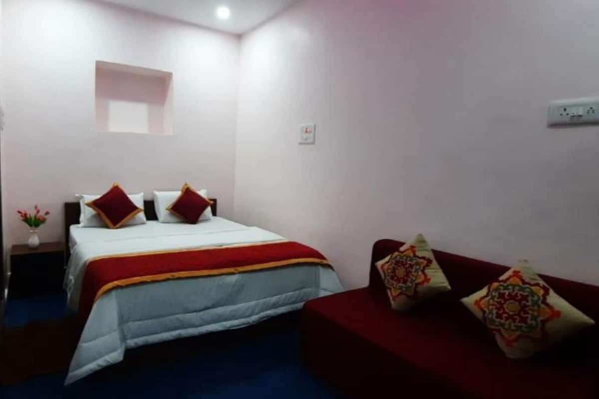 A bedroom with a bed, a red sofa, and a nightstand with a vase of flowers.