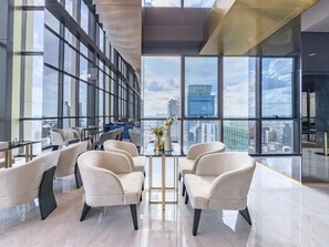A modern interior with large windows, a seating area with chairs, and a view of the cityscape.