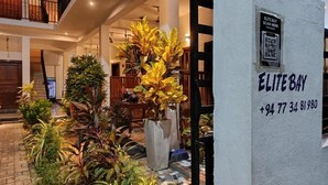 Een moderne hotelingang met een wit receptiebalie, een QR-code om te scannen, en de naam 'ELITE BAY' met een telefoonnummer.