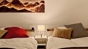 Et hotelværelse med to senge, et natbord med lampe og et vægmaleri der viser bjerge.