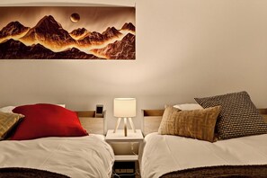 Une chambre d’hôtel avec deux lits, une table de chevet avec une lampe et une œuvre d’art accrochée au mur représentant des montagnes.