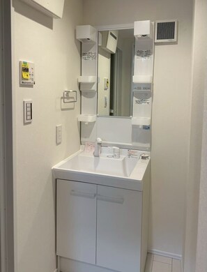 Une salle de bain avec un lavabo blanc, un miroir et un appareil de ventilation fixé au mur.