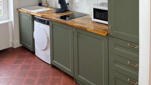 Une cuisine compacte avec des meubles de couleur verte, un plan de travail en bois, un lave-linge, un four à micro-ondes et un évier avec un robinet.