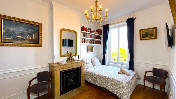 Une chambre à coucher avec un lit, une cheminée, une bibliothèque et une grande fenêtre avec des rideaux.
