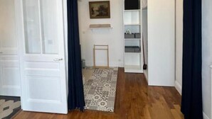 Un couloir avec un plancher en bois, des murs blancs et des rideaux noirs. Un tapis à motifs recouvre le sol et un tableau est accroché au mur.