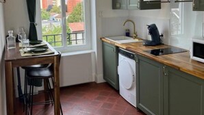 Une cuisine compacte équipée d’un lave-linge, d’un évier et d’une fenêtre donnant sur les bâtiments environnants.