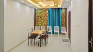 Un coin repas comprenant une table et des chaises, un ventilateur de plafond et une vue sur l’extérieur à travers des rideaux.