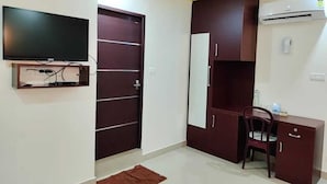 Une pièce avec un téléviseur fixé au mur, une armoire à plusieurs portes, un bureau avec une chaise et un appareil de climatisation fixé au mur.