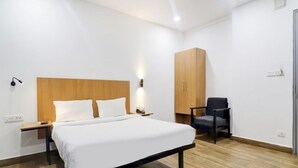 Ett hotellrum med en säng som har en sänggavel i trä, ett litet bord vid sängen med en lampa, en stol och en garderob.
