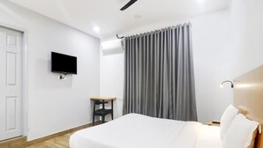Ett hotellrum med en säng, en tv som är monterad på väggen, ett skrivbord och ett fönster med gardiner.