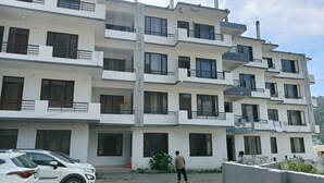 A multi-story residential building with balconies, a gravel driveway, and parked cars. - Hotel Dark Clouds (Sukha)