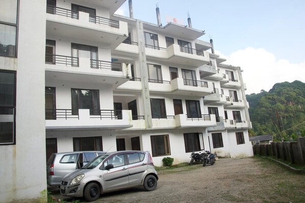 Un edificio de varios pisos con balcones, autos estacionados y una motocicleta.