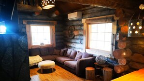L’intérieur d’un chalet confortable, avec un plancher en bois, un canapé, une table et deux fenêtres qui laissent entrer la lumière naturelle.