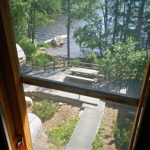 Une vue depuis une fenêtre donnant sur une terrasse en bois, avec une rivière et des arbres en arrière-plan.