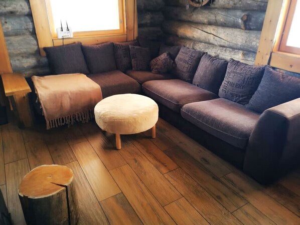 L’intérieur d’un chalet confortable, avec un canapé d’angle, un petit pouf rond et un plancher en bois.