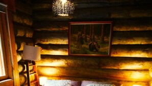 Une pièce chaleureuse dans un chalet en rondins, avec un lit, une lampe et un tableau accroché au mur.