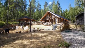 Une cabane rustique en rondins de bois, dotée d’une terrasse en bois et d’un espace extérieur couvert.
