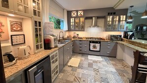 A modern kitchen with granite countertops, stainless steel appliances, and patterned tile flooring. - Villa Amarela - Itacimirim - Bahia - 5 suítes (Camaçari)