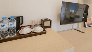 Een receptiebalie in een hotel, met een flatscreen-tv, een koffiezetapparaat, waterflesjes en een dienblad met borden en bekers.