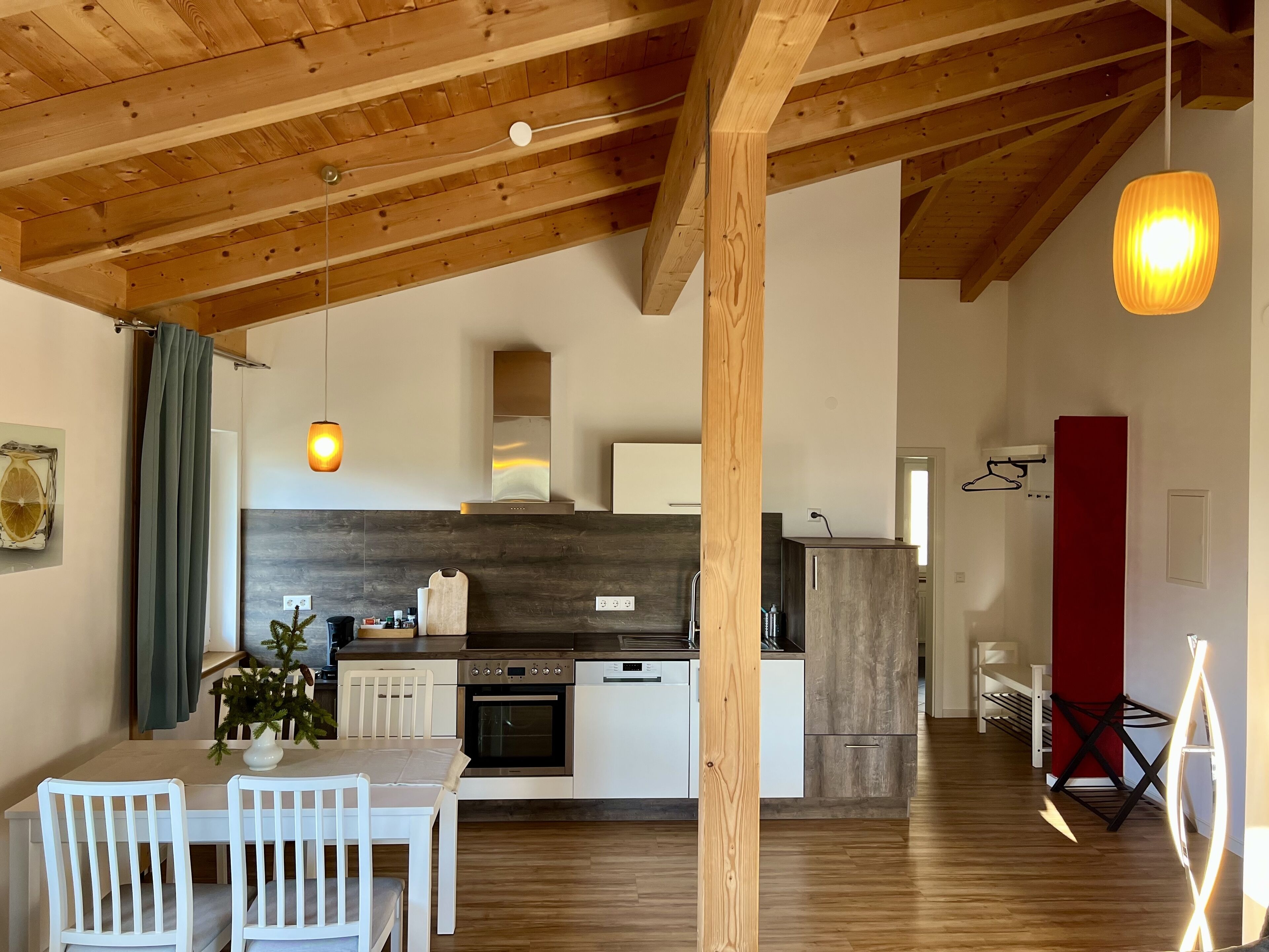 Une cuisine moderne avec des poutres en bois, un coin repas avec des chaises blanches et un luminaire suspendu.