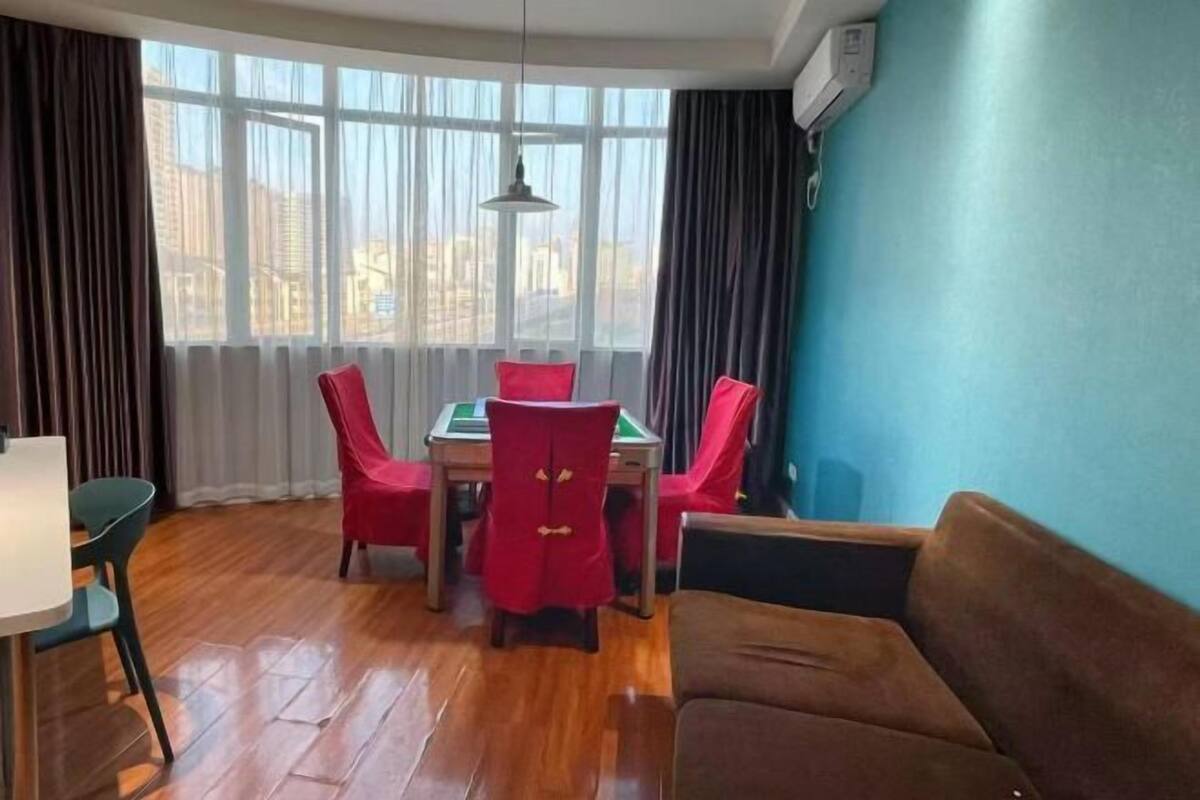 A room with a table and chairs, a sofa, a window with curtains, and an air conditioning unit.