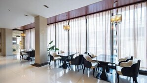 Un comedor moderno con una mesa grande y sillas, ventanas amplias con cortinas translúcidas e iluminación colgante.