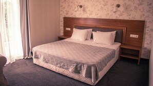 Camera d'albergo con un letto grande, una testiera in legno, due comodini e un motivo floreale sulla carta da parati.