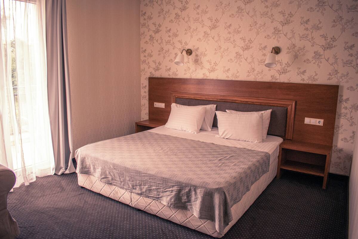 Een hotelkamer met een groot bed, een houten hoofdbord, twee nachtkastjes en een behang met een bloemenpatroon.
