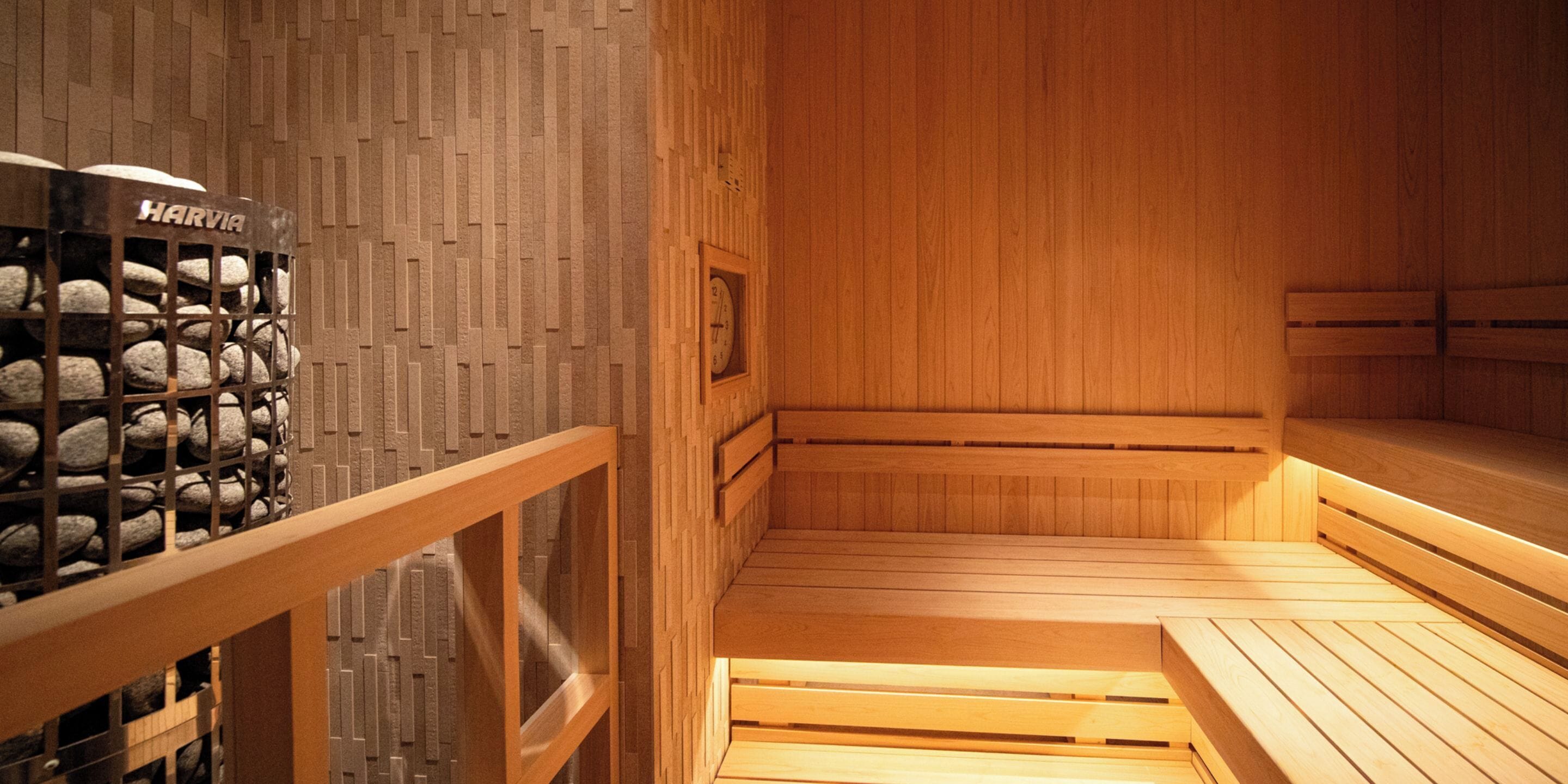 A wooden sauna with benches, a Harvia sauna heater, and a wall with a geometric pattern.